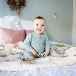 Smiling baby sitting on farm animal print waffle blanket on a bed.