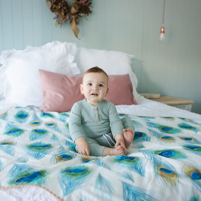 Peacock print blanket spread on bed with baby sitting on in