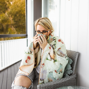 Lady drinking cup of tea on verandah with waffle blanket around her shoulders to stay warm