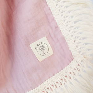 Close up of dusty pink baby swaddle showing 8crew logo and fringing