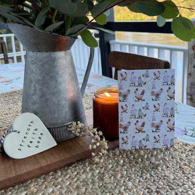 Nabiac Friends farm animal card displayed on table with candle, plant and water background.