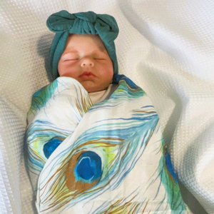 Baby wrapped in swaddle with peacock feather print.